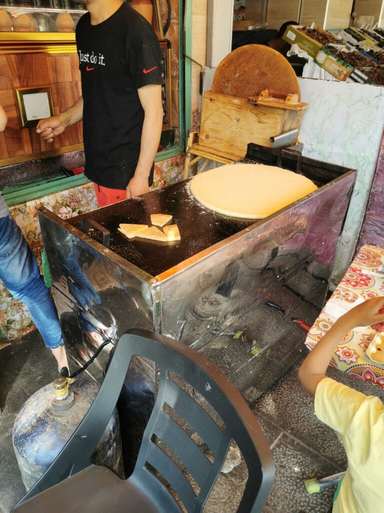 A man in a black shirt stands near a street food stall in Morocco, showcasing traditional harcha bread.