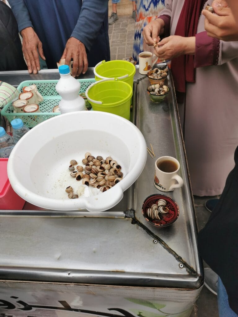 A woman dressed in black observes street food vendors in Essaouira, Morocco, where snails are a popular local dish.