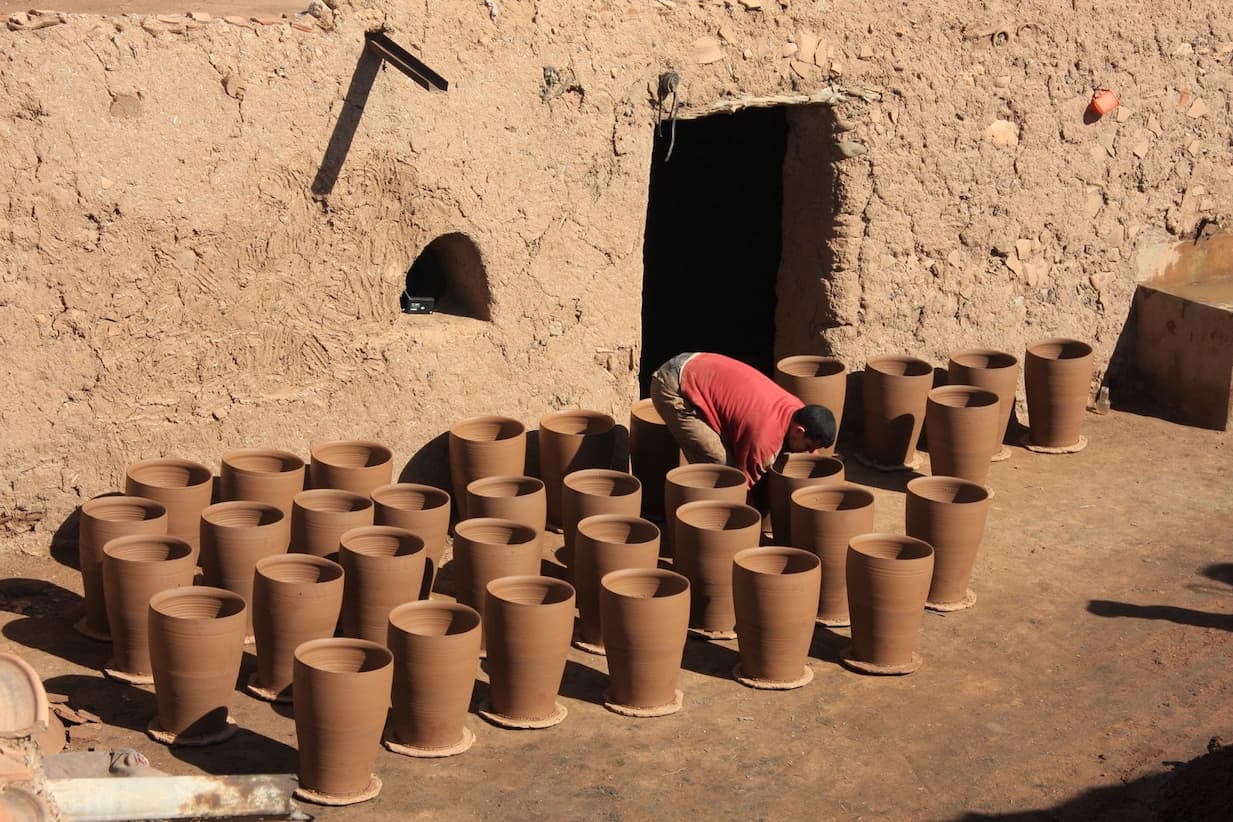 A potter in Morocco is working on his pottery made of clay, at the door of a rural house.