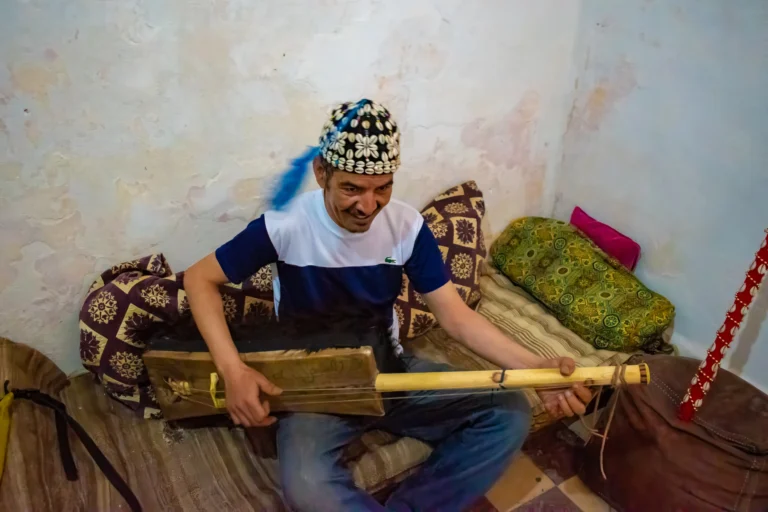 A gnawa musician playing the guembri with traditional hat