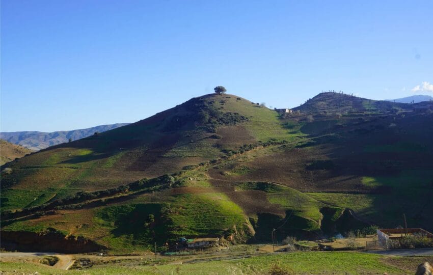 Lush green and red clay mountains of the Rif region surrounding a rural Moroccan village.