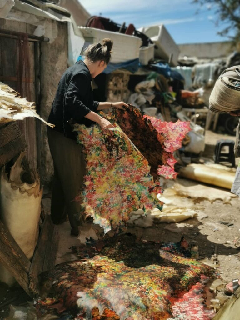 A visitor examining a large, multicolored hand-dyed leather skin during an immersive tour of a local tannery in Essaouira.