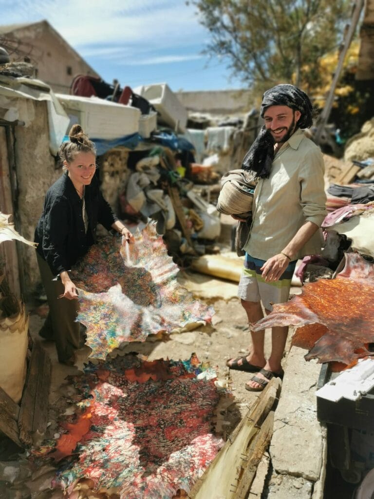 Visitors inspecting colorful, handmade leather skins at the traditional tannery in Essaouira.